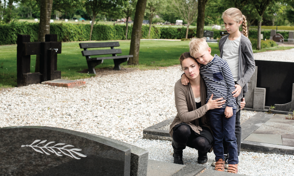 A mother hugs her children by a gravesite