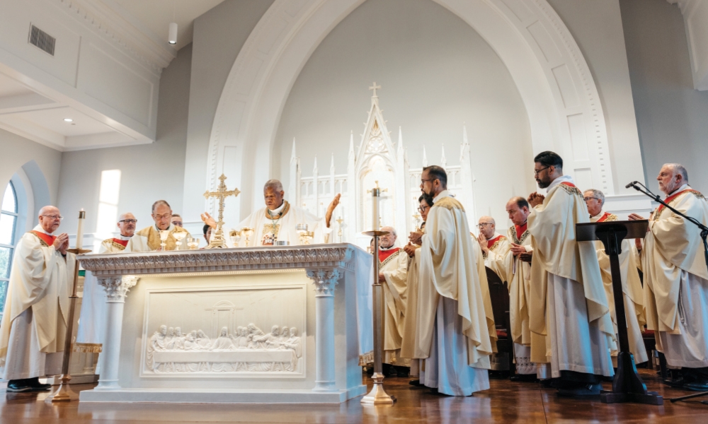 Bishop Fabre-Jeune consecrating hosts during Mass, surrounded by priests