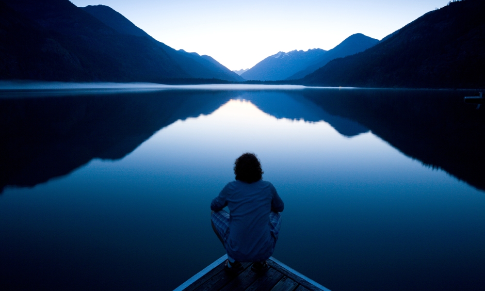 Person contemplating a still lake