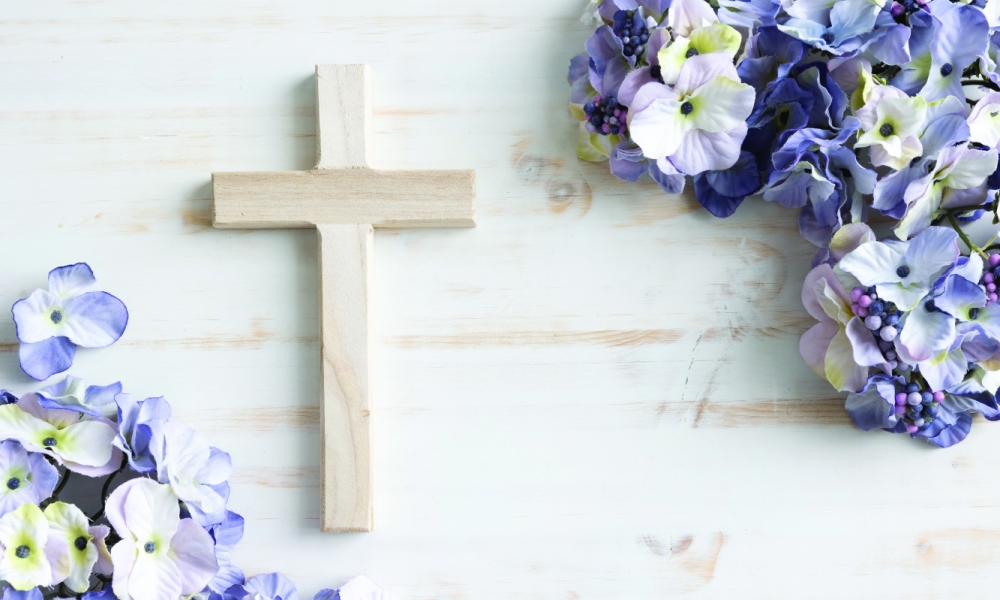 A wooden cross surrounded by purple and white flowers
