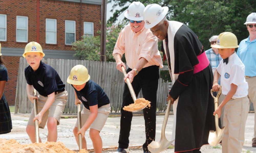 Bishop Jacques Fabre-Jeune with kids in hard hats digging dirt