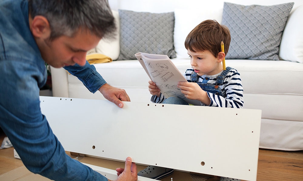 Child holding instruction manual and helping father build furniture