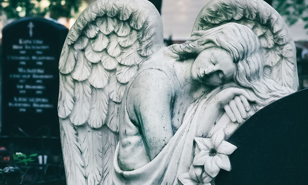 Angel statue resting over a headstone in a cemetery